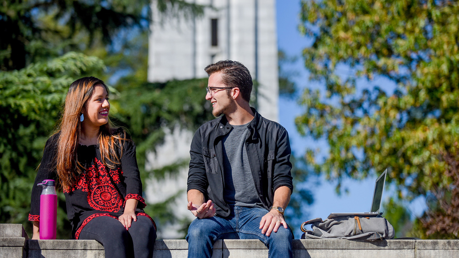 two students sitting on ledge in front of belltower