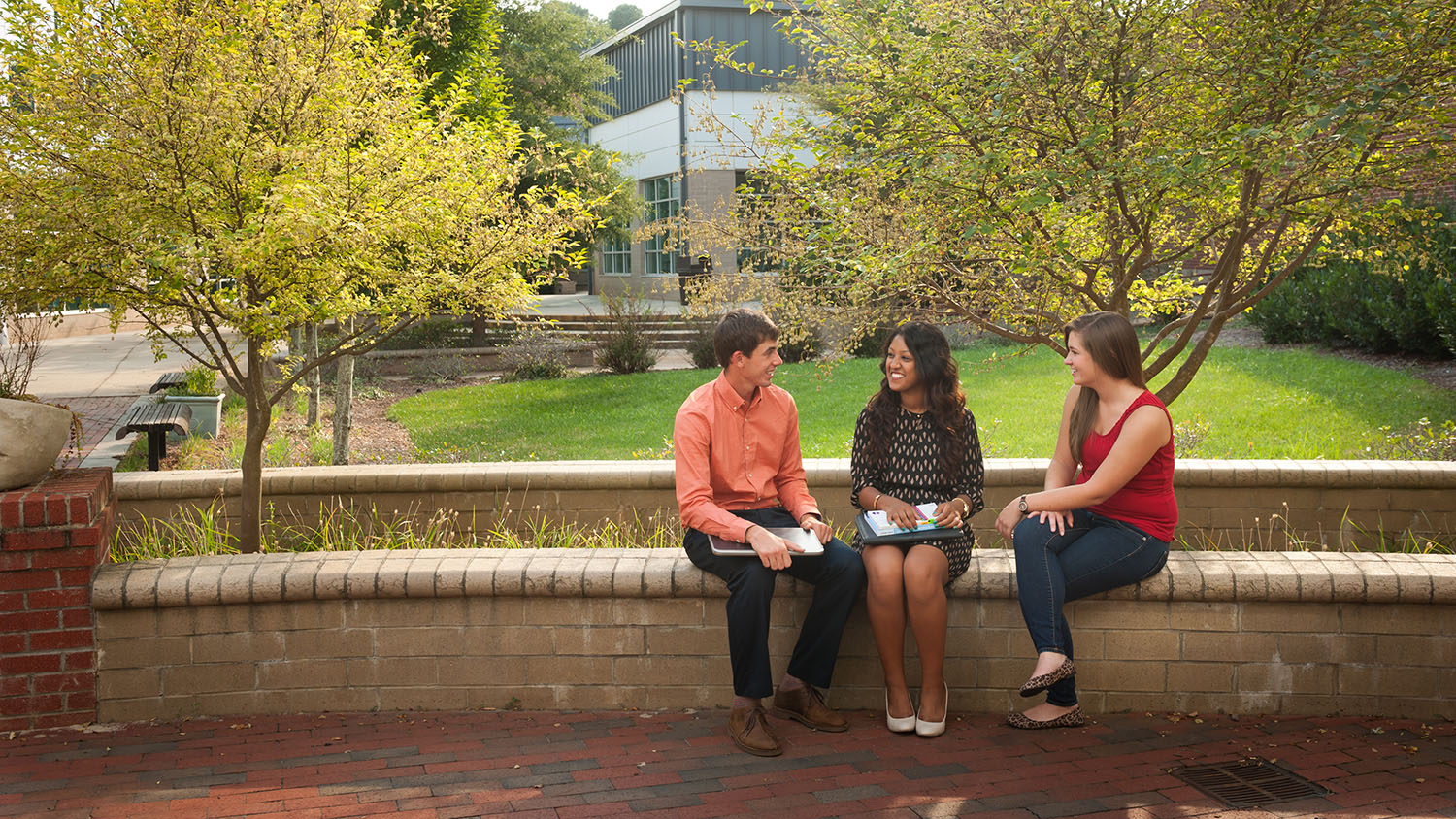 three students sitting on brick ledge