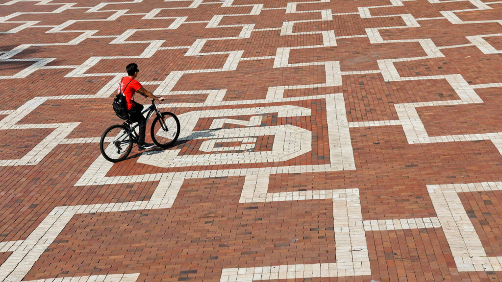 student rides bike across the brickyard