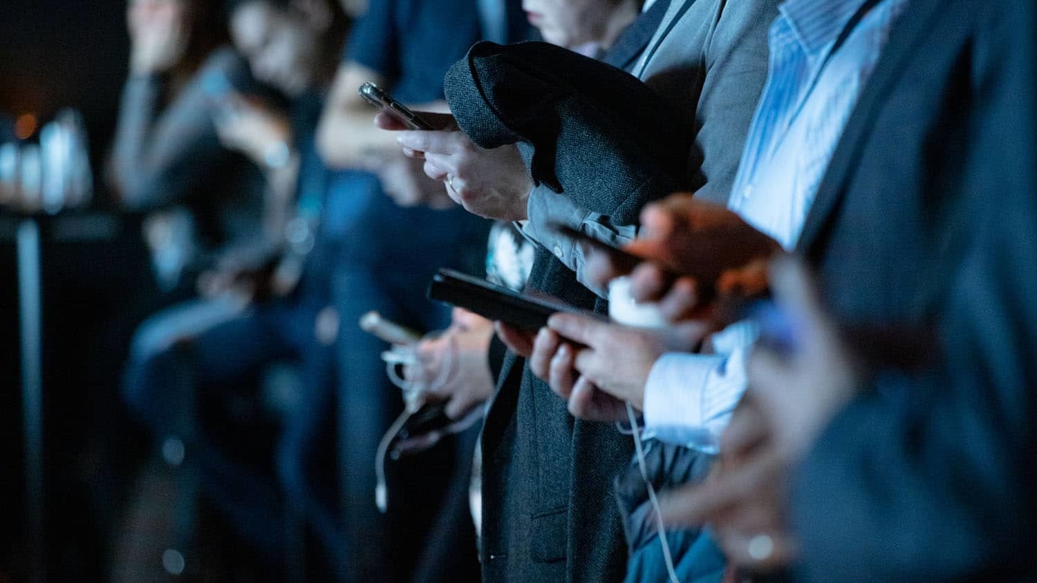 a crowd of people stand looking at their smartphones