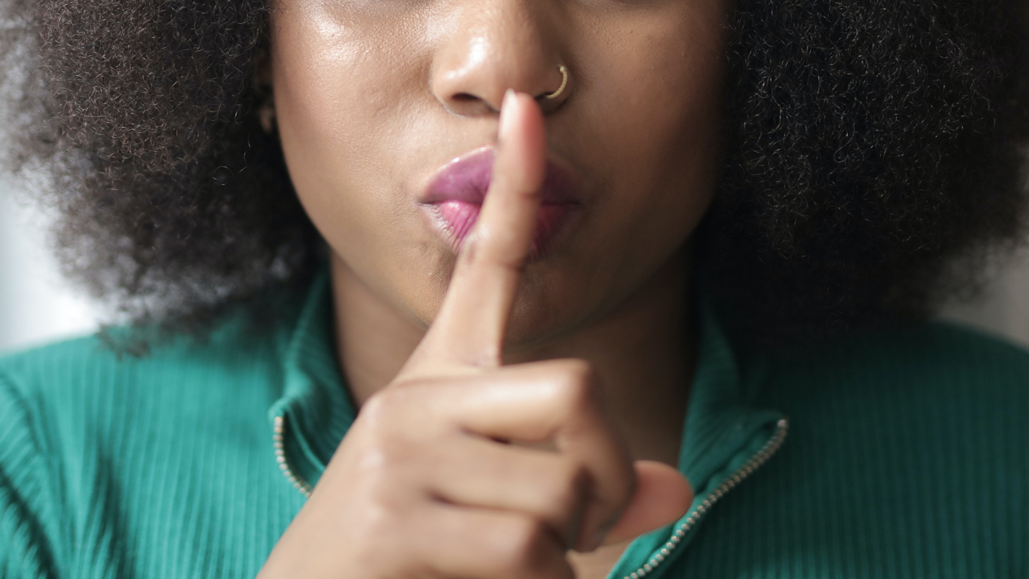 A woman holds a finger over her mouth, "shh"