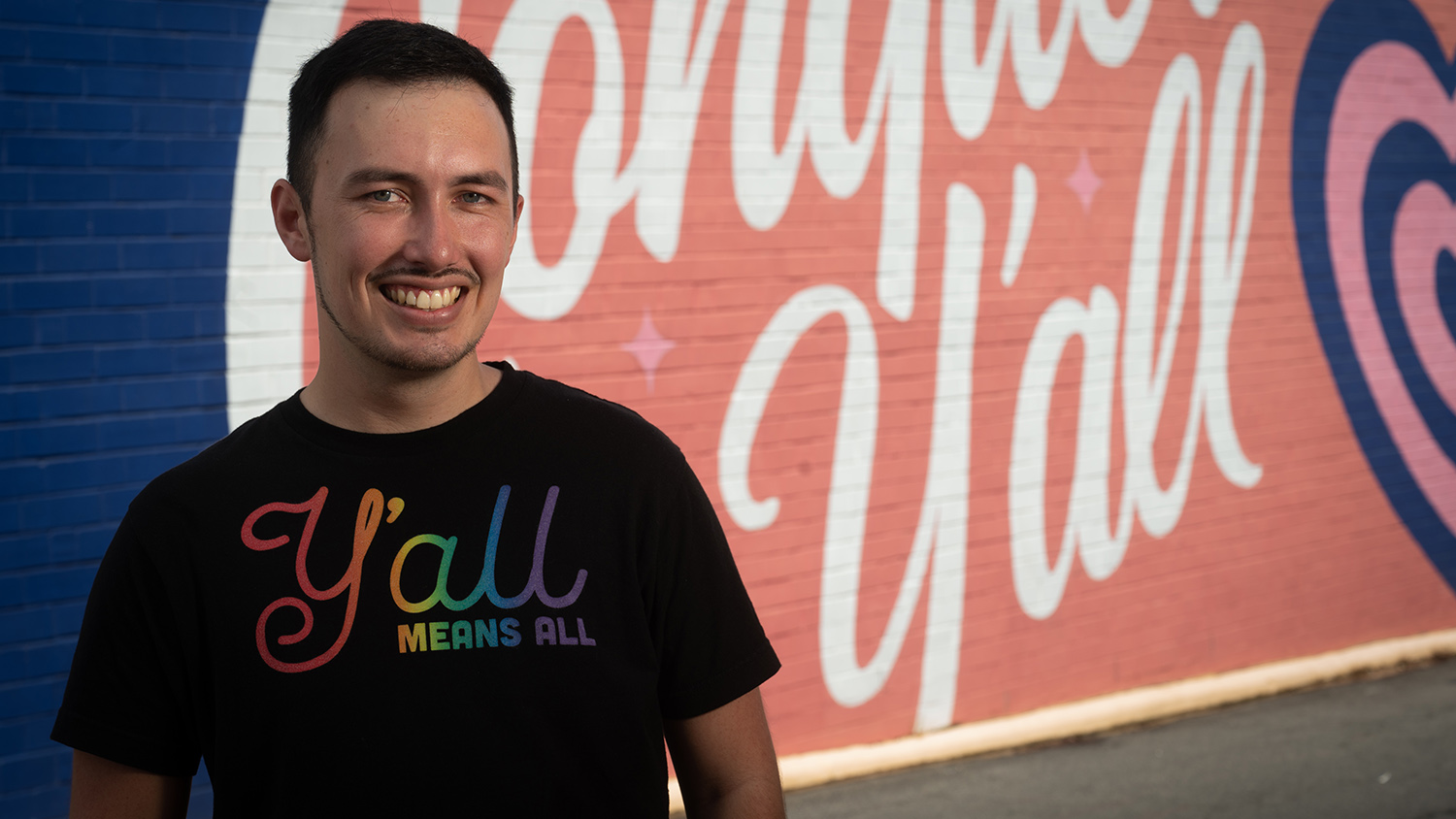 Brody McCurdy stands in front of a mural. The word "y'all" can be seen in the background.