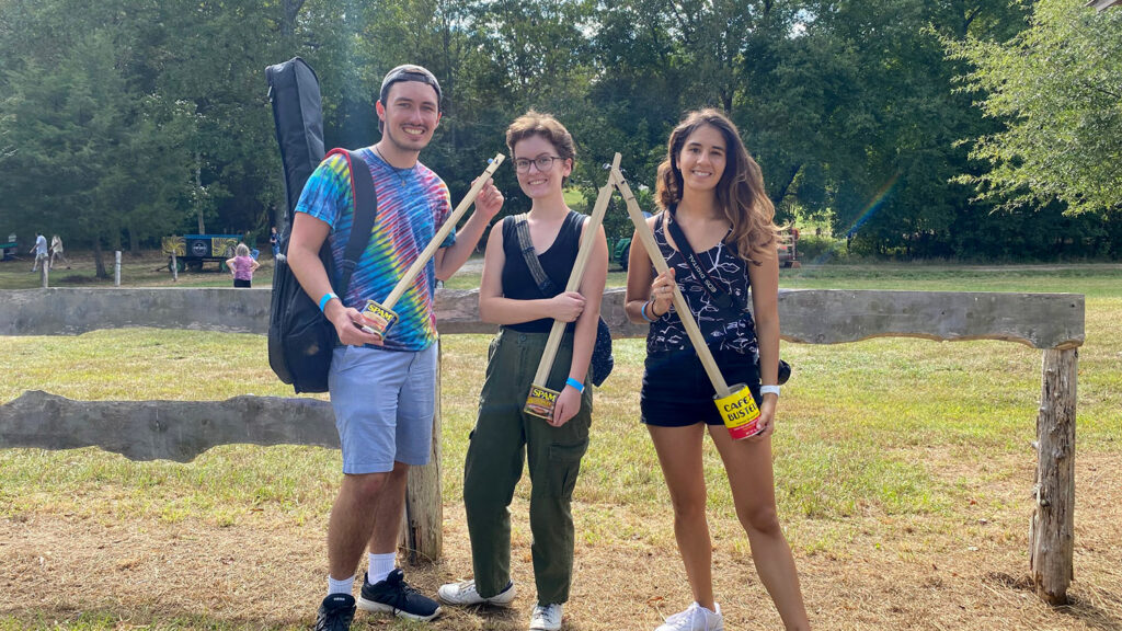 Three people hold sticks with cans attached to one end. 