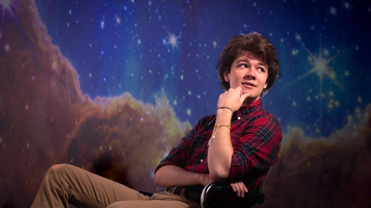 Kevin Cabral sits in a chair, in front of an image from space