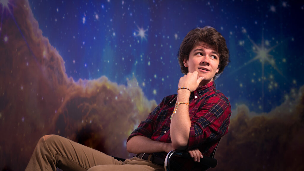 A student sits in a chair, in front of a large image from space