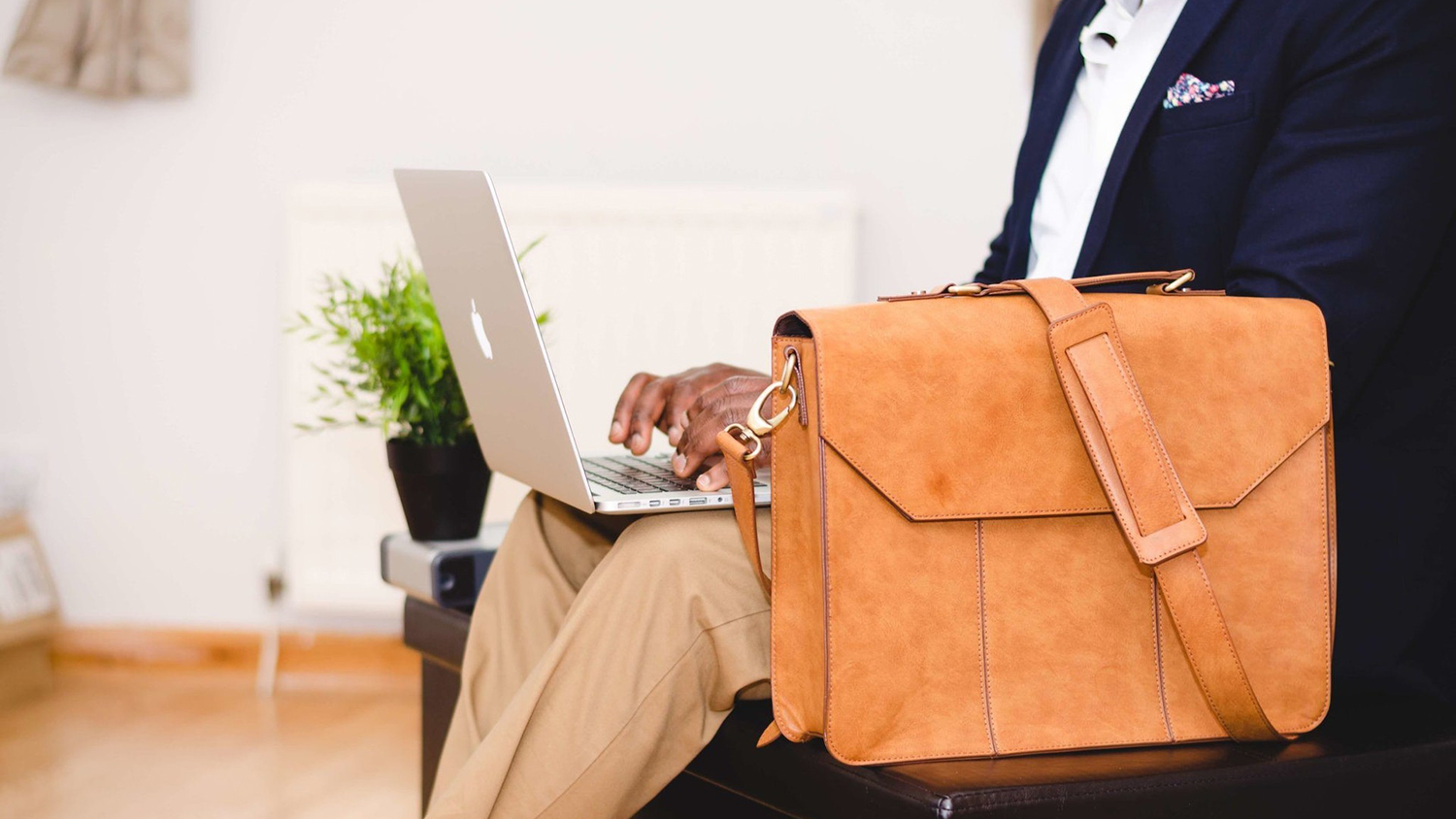 A person types on a laptop, sitting next to a briefcase