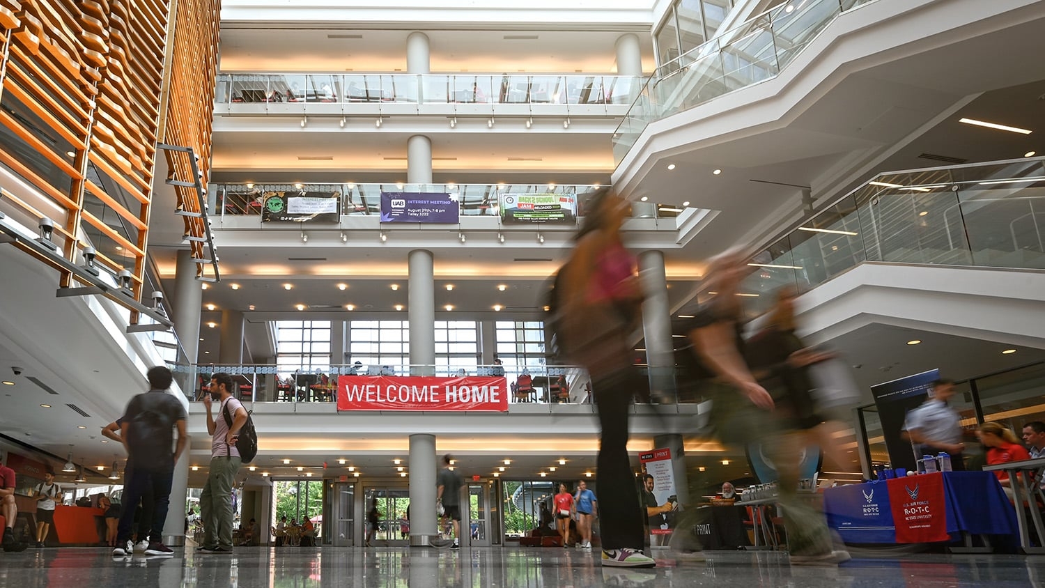 People walking appear blurred in this picture, taken in Talley Student Union. Students wear backpacks, and informational booths line the union's lobby.