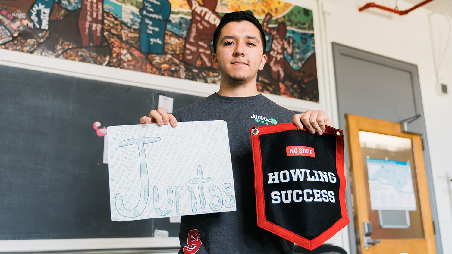Sebastian Rios holds a white sign that reads "Juntos" in handwritten green letters and a red, black and white pennant that reads "Howling Success" in the other hand