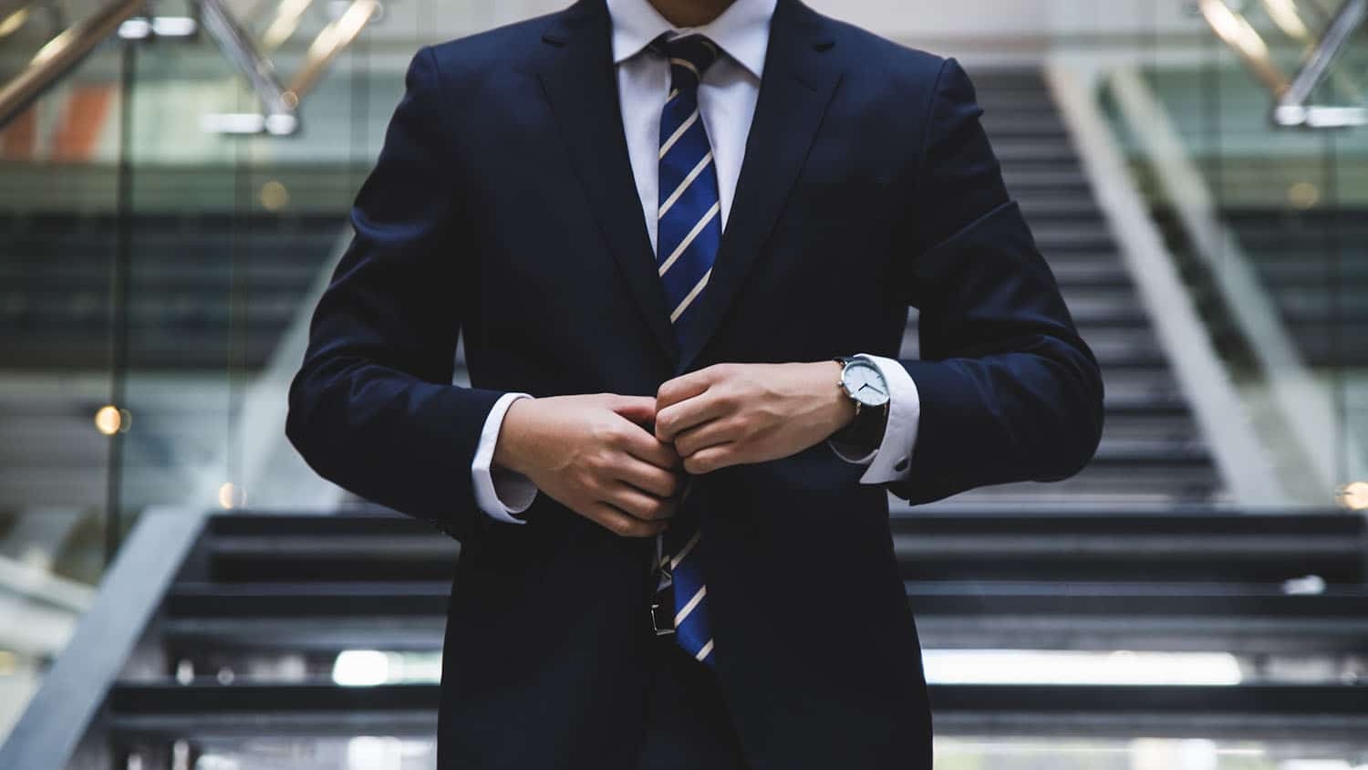 photo shows a man from the neck to the waist. He is wearing a suit and tie and is buttoning his coat. the photo suggests a business person preparing to go into a meeting or interview.