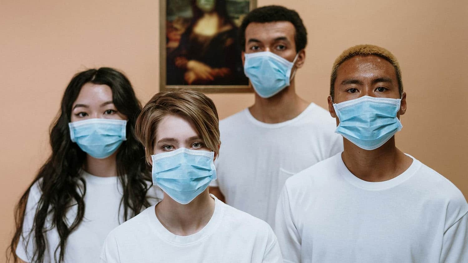 four young adults of different racial backgrounds stand together wearing masks that cover their nose and mouth.