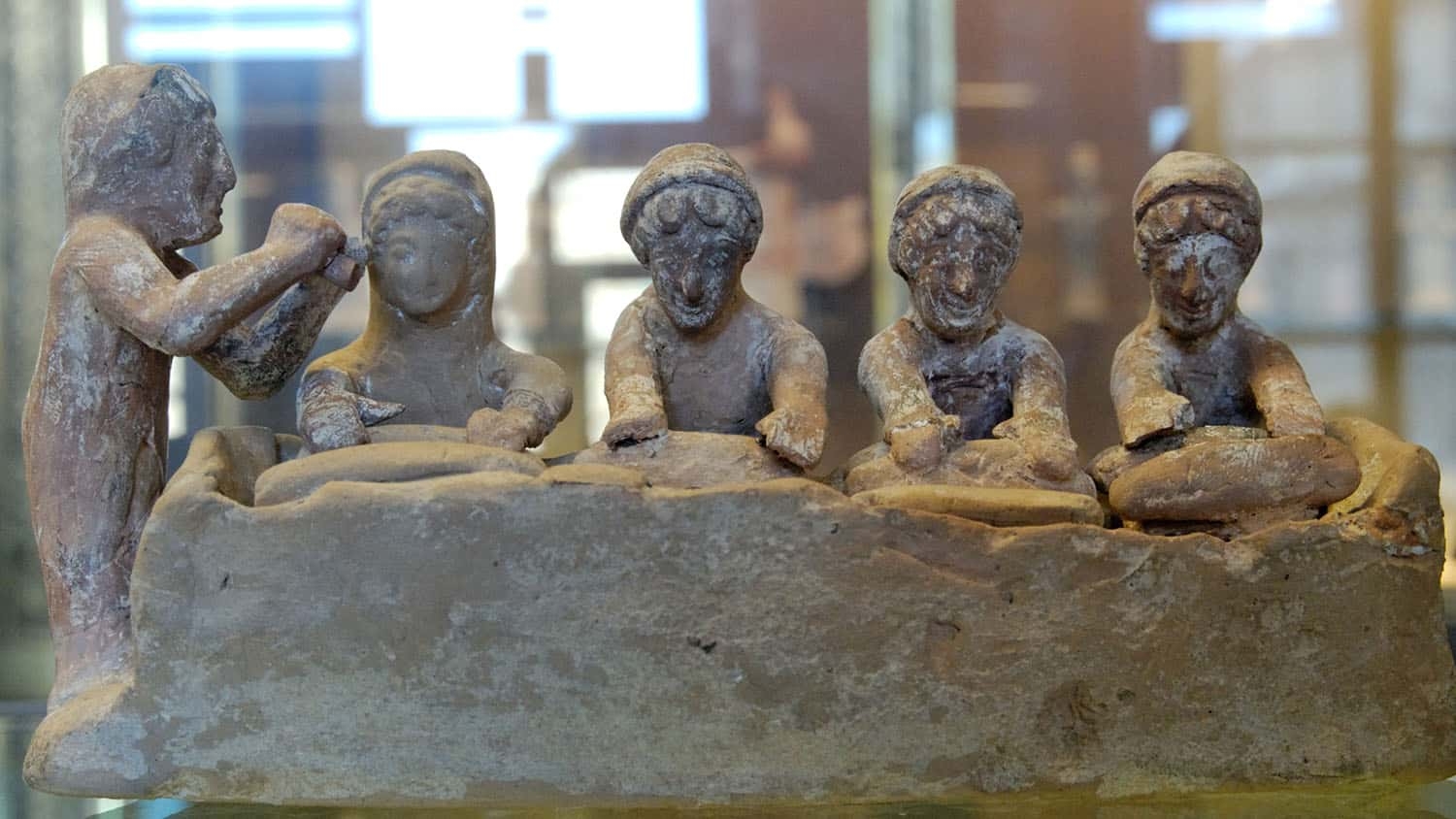 a terracotta sculpture shows four people kneading dough on a table while a fifth person looks on