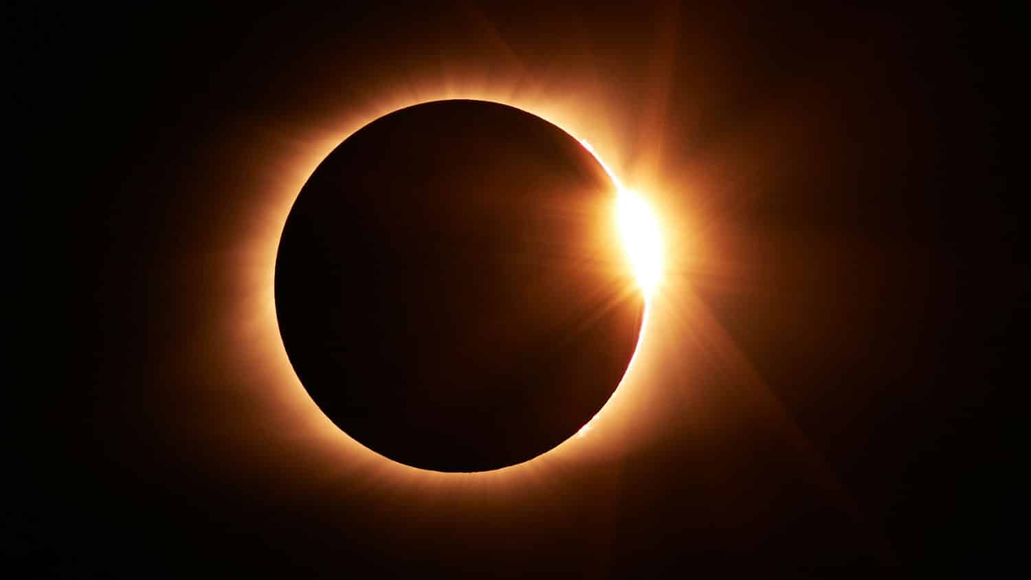 photo of an eclipse shows a black sphere against a black sky, surrounded by a thin ray of golden light